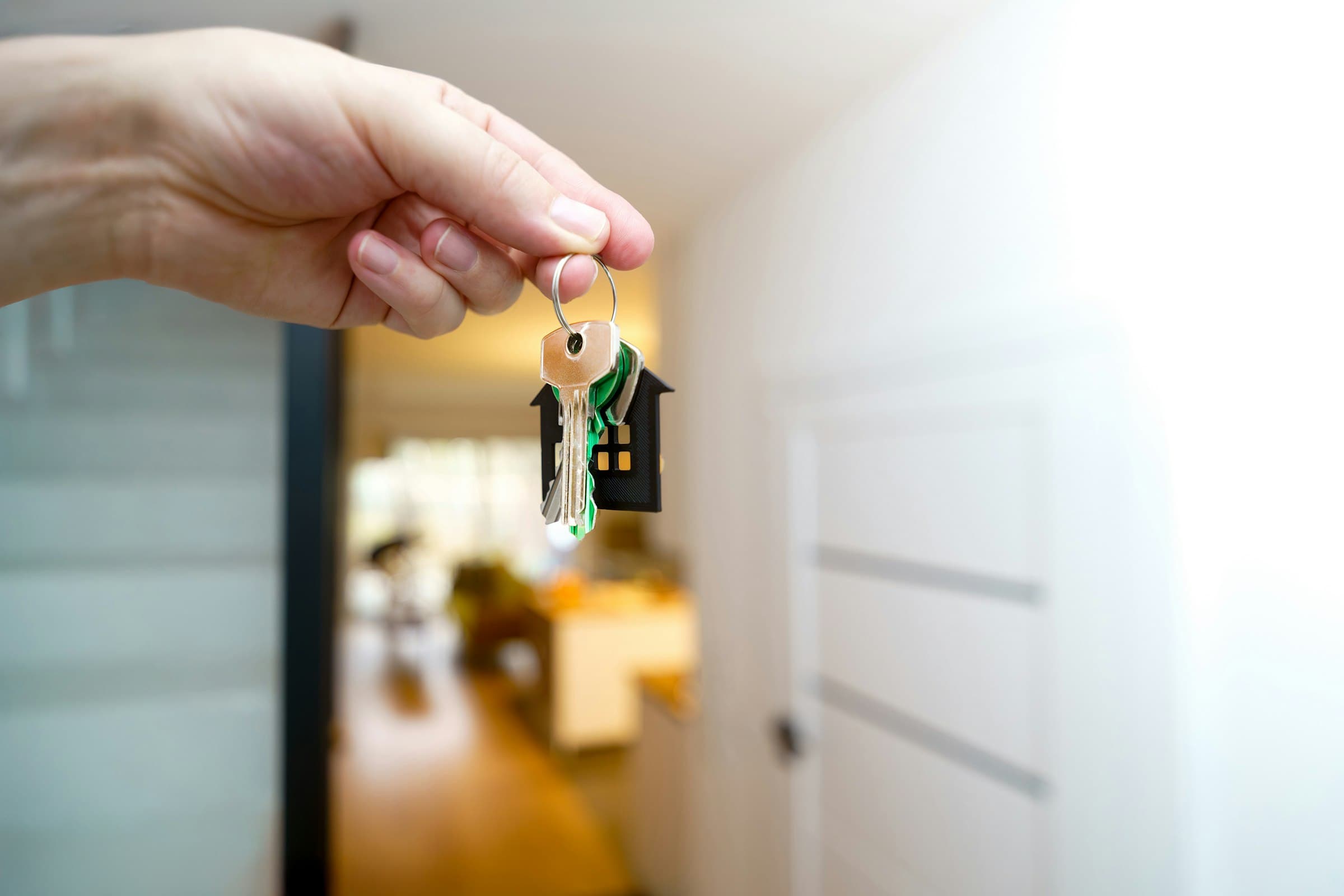Hand holding house keys at the front door of a home
