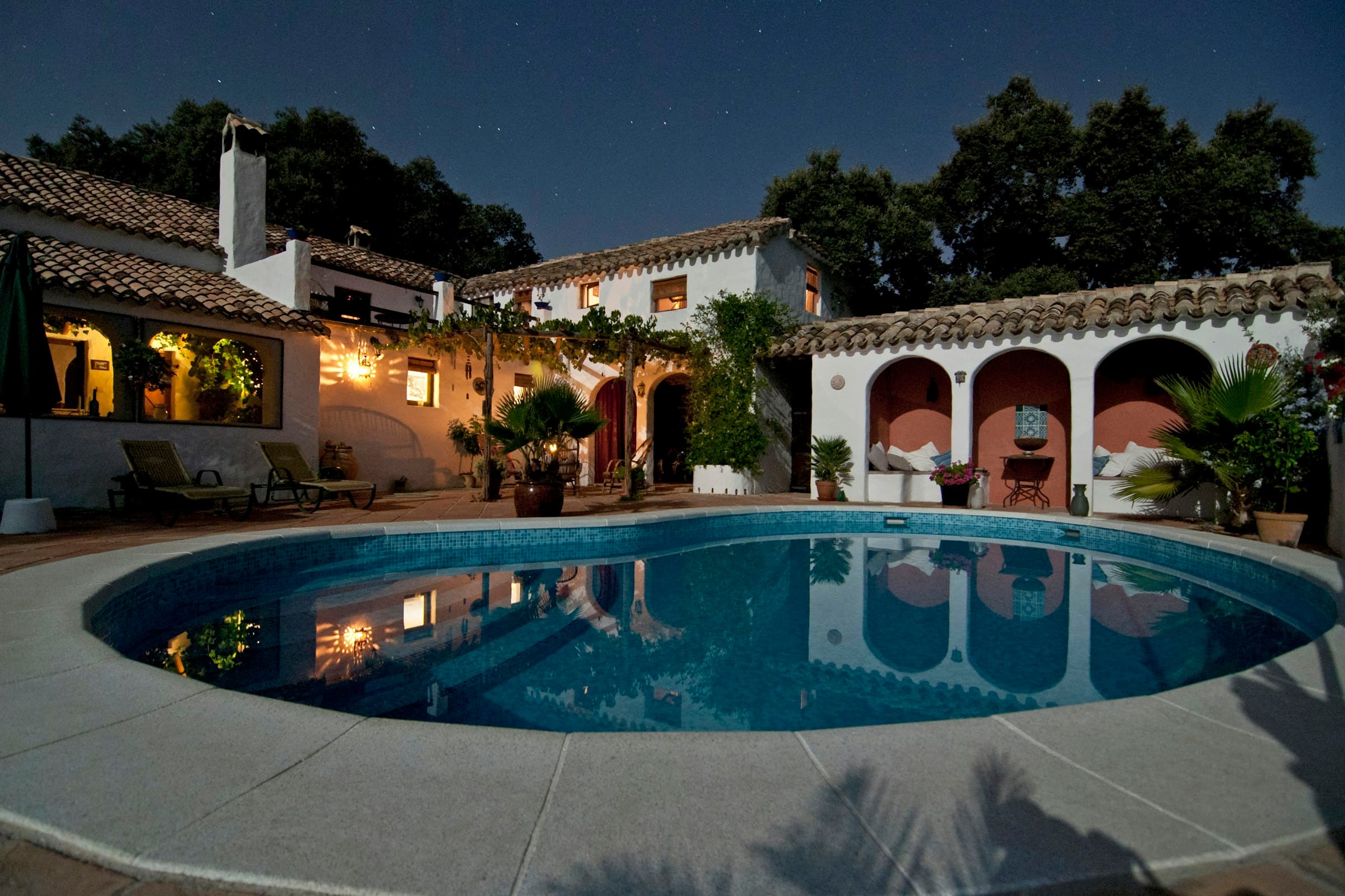 Spanish finca lit warmly at dusk with round pool in the foreground